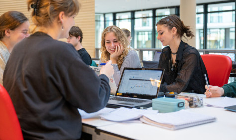 vier studentes zijn lachend aan het werk op hun laptop