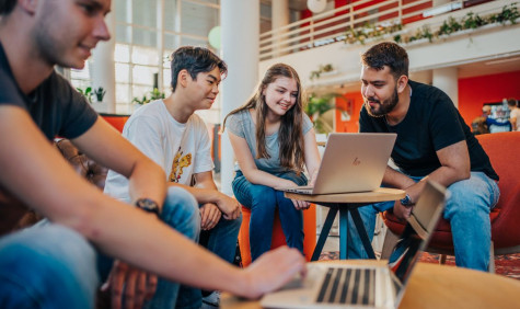 Studenten achter laptops aan lage tafels in een open ruimte in een instelling