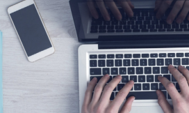Man aan laptop met mobiel van bovenaf gefotografeerd