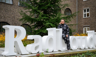 Alexandra van Huffelen zittend op witte Radboud letters in de tuin van het Berchmanium in Nijmegen